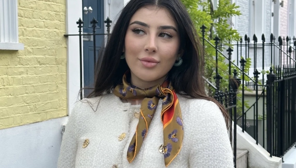 Woman wearing Bird In Flight silk scarf in gold colourway tied at the neck with cream bouclé jacket on a London street