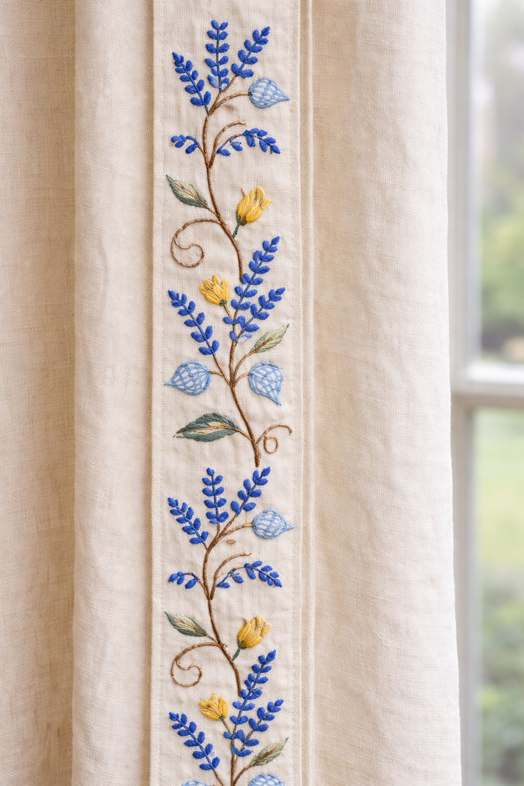 Close-up of cream linen curtain with crewel embroidered botanical border featuring blue ferns, yellow tulips, and latticed seed pods